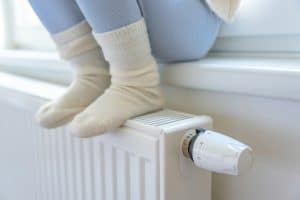 Feet of little girl in warm white socks. Child sitting and warming up from the heating radiator